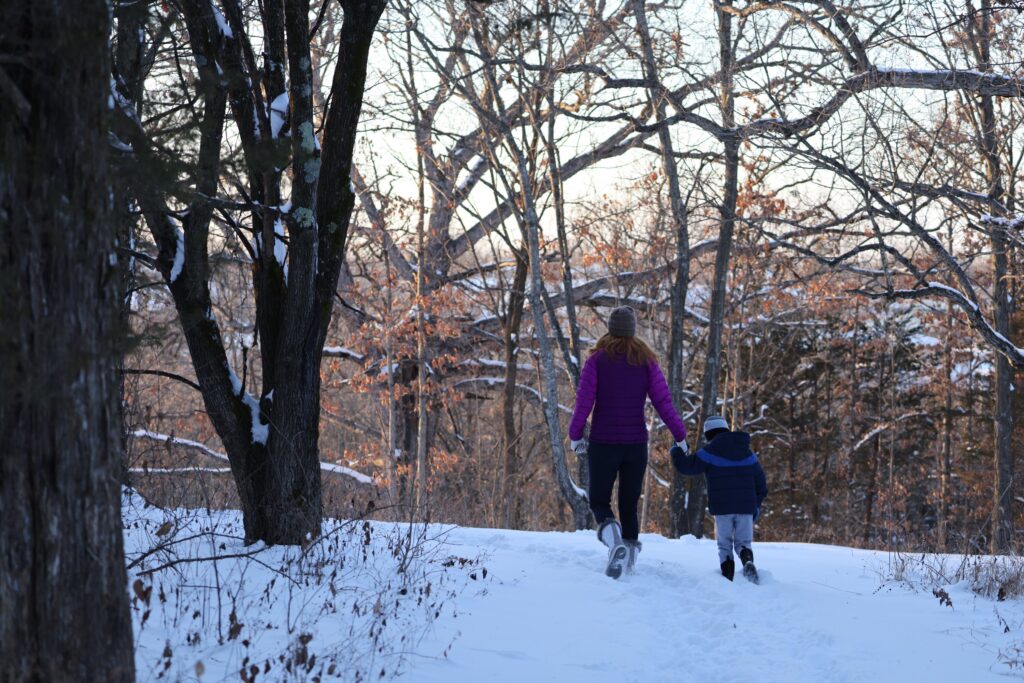 photo of adult and child walking in snowy woods